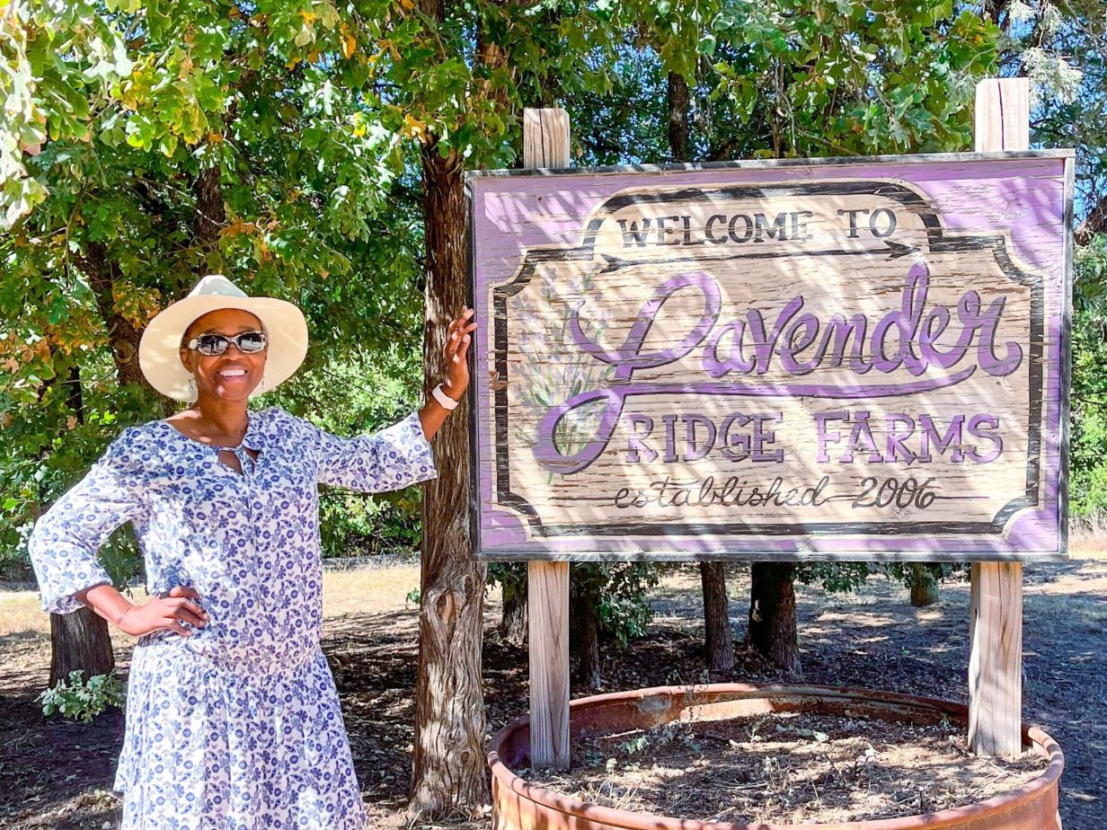 A woman standing next to a sign that reads “Lavender Ridge Farms.”