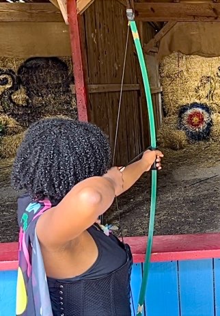 Renaissance fair visitor draws a bow and aims an arrow at an archery target on a hay bale at Scarborough Renaissance Festival, one of the unique-things-to-do-in-dfw.