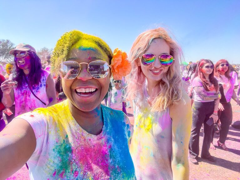 Two young ladies covered in bright colored chalk and enjoying themselves at the Holi Dallas Festival. Another reason why dallas is worth visiting.