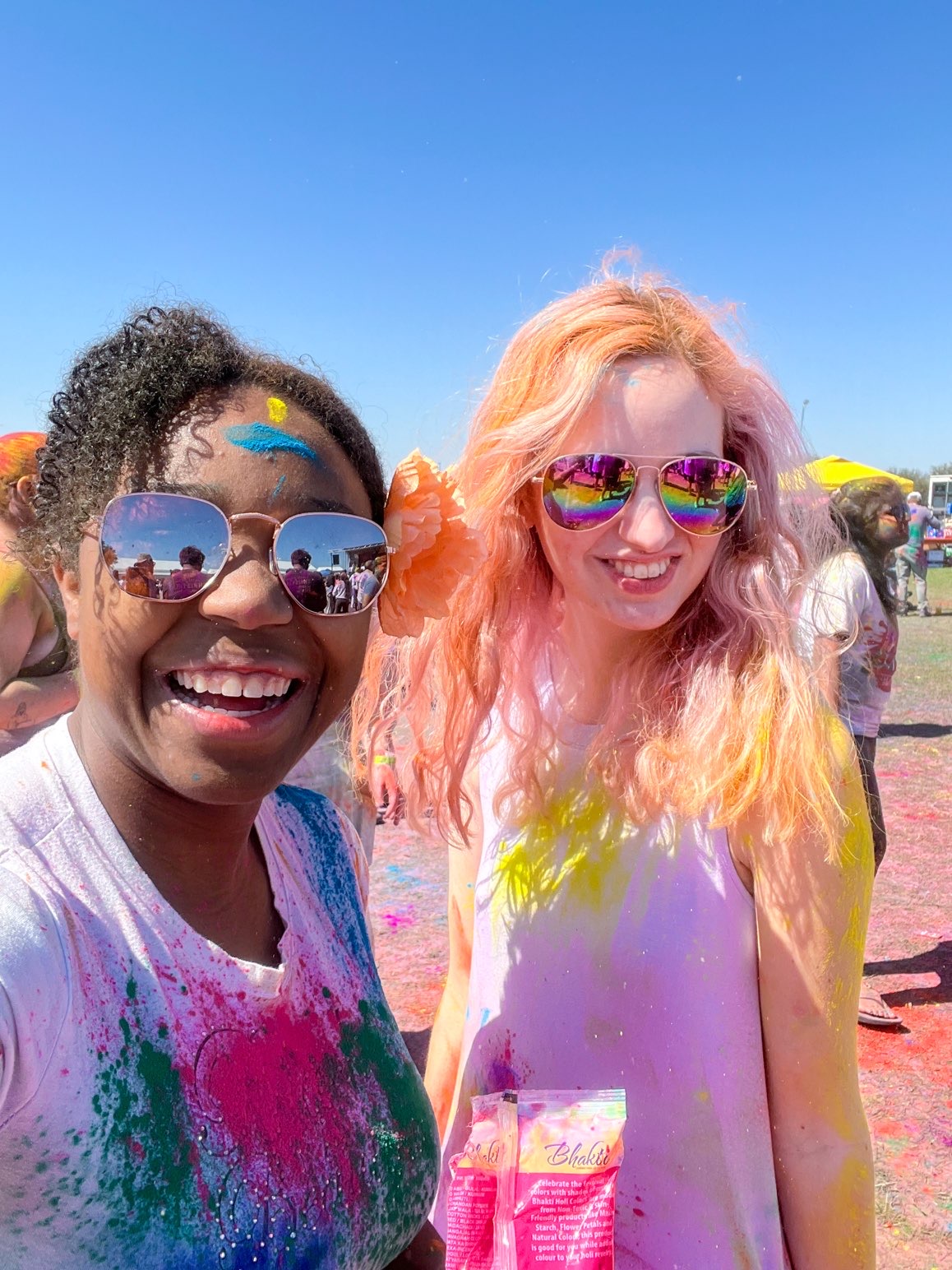 Two friends dance and celebrate amid clouds of colorful powder at a Holi celebration in DFW, one of the vibrant unique-things-to-do-in-dfw.