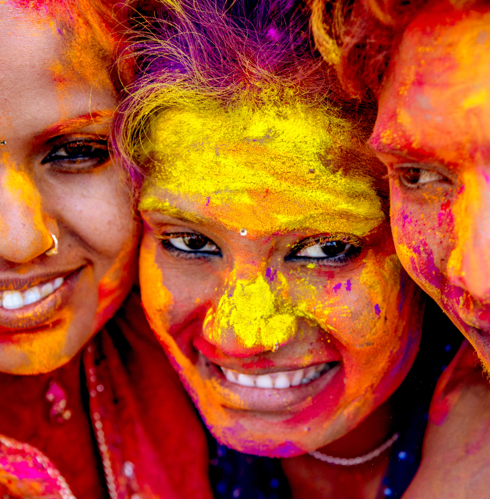 3 young ladies covered in orange, and yellow chalk smiling gleefully; Dallas Festival