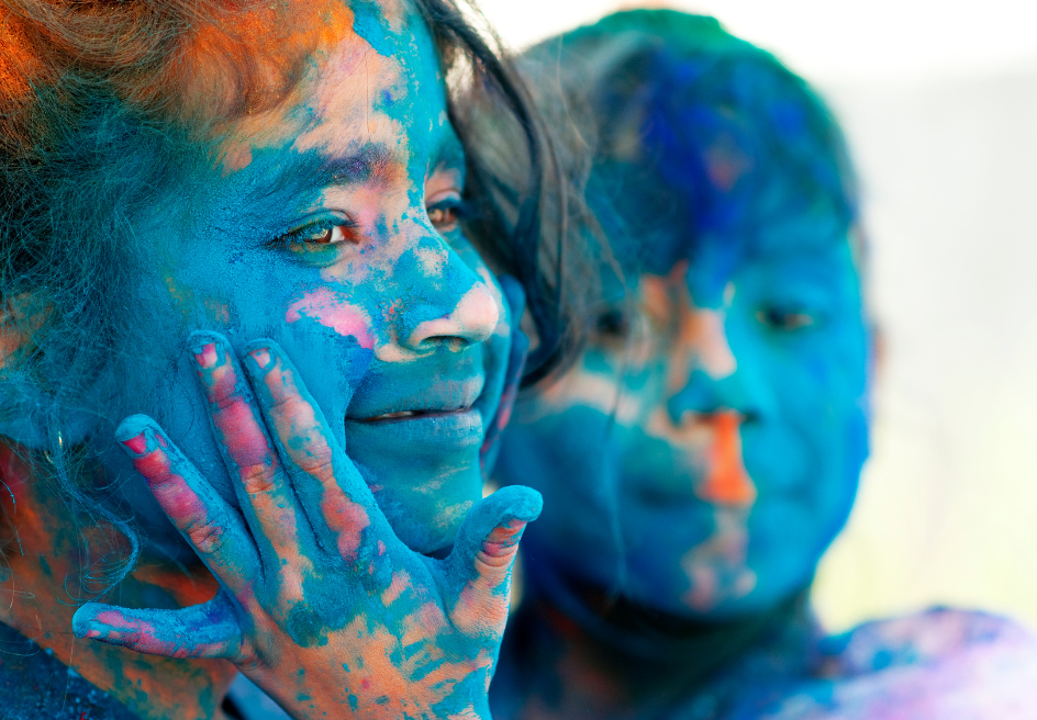 Two young children, a boy and a girl are covered with blue chalk . The young boy has his hand on the little girl's face, and both are slightly smiling at the Holi Dallas Festival