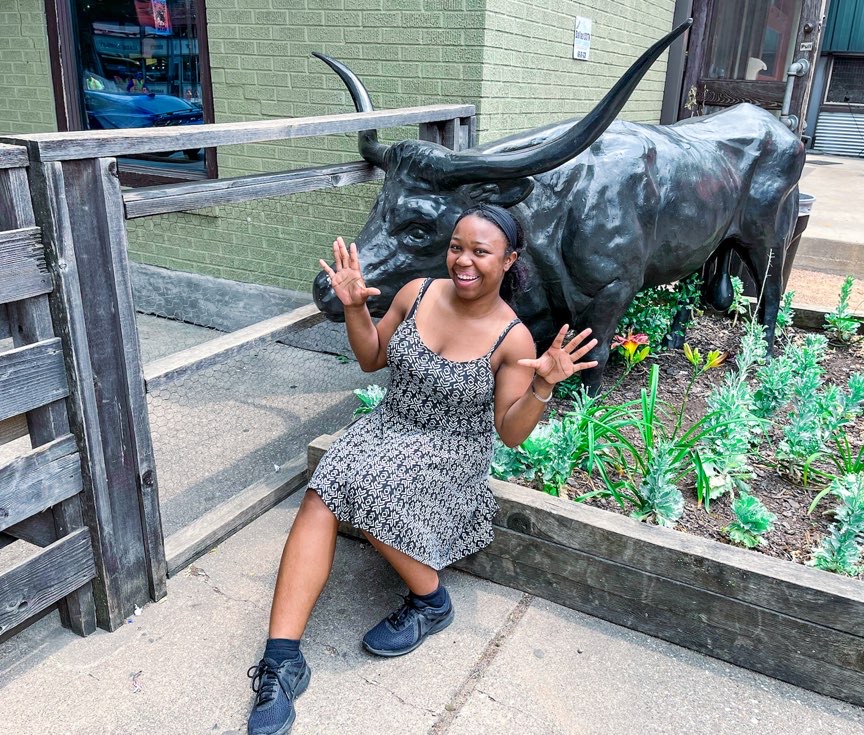 Woman sitting on curb in front of steer sculpture at Pecan Lodge in Deep Ellum
