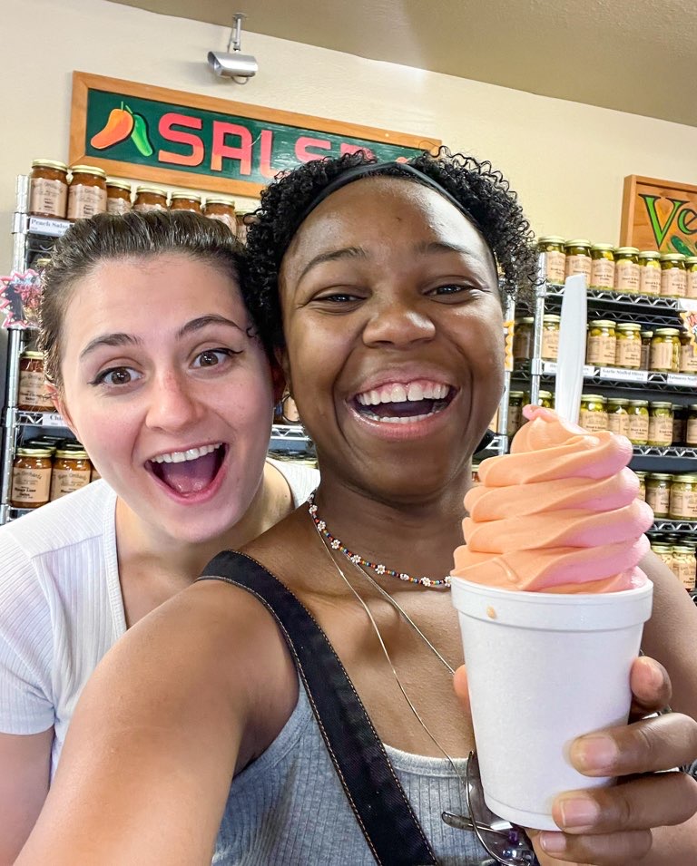 Two smiling young women holding up a large cup of swirled peach ice cream at Ham Orchards.