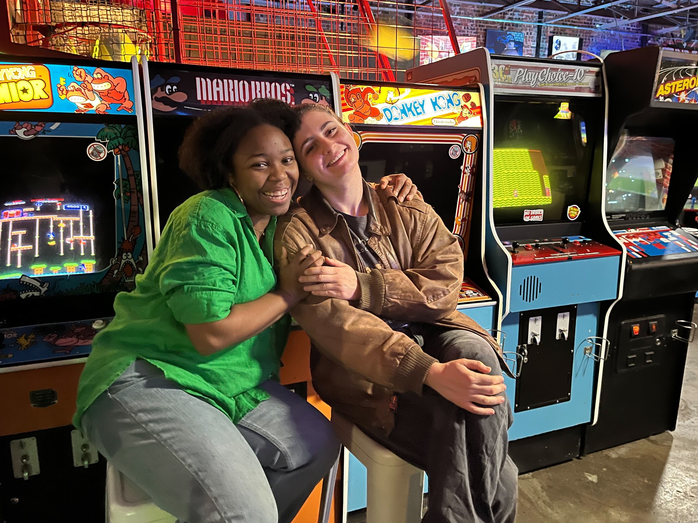 Two friends pose in front of retro arcade games at one of the best indoor activities in Dallas.