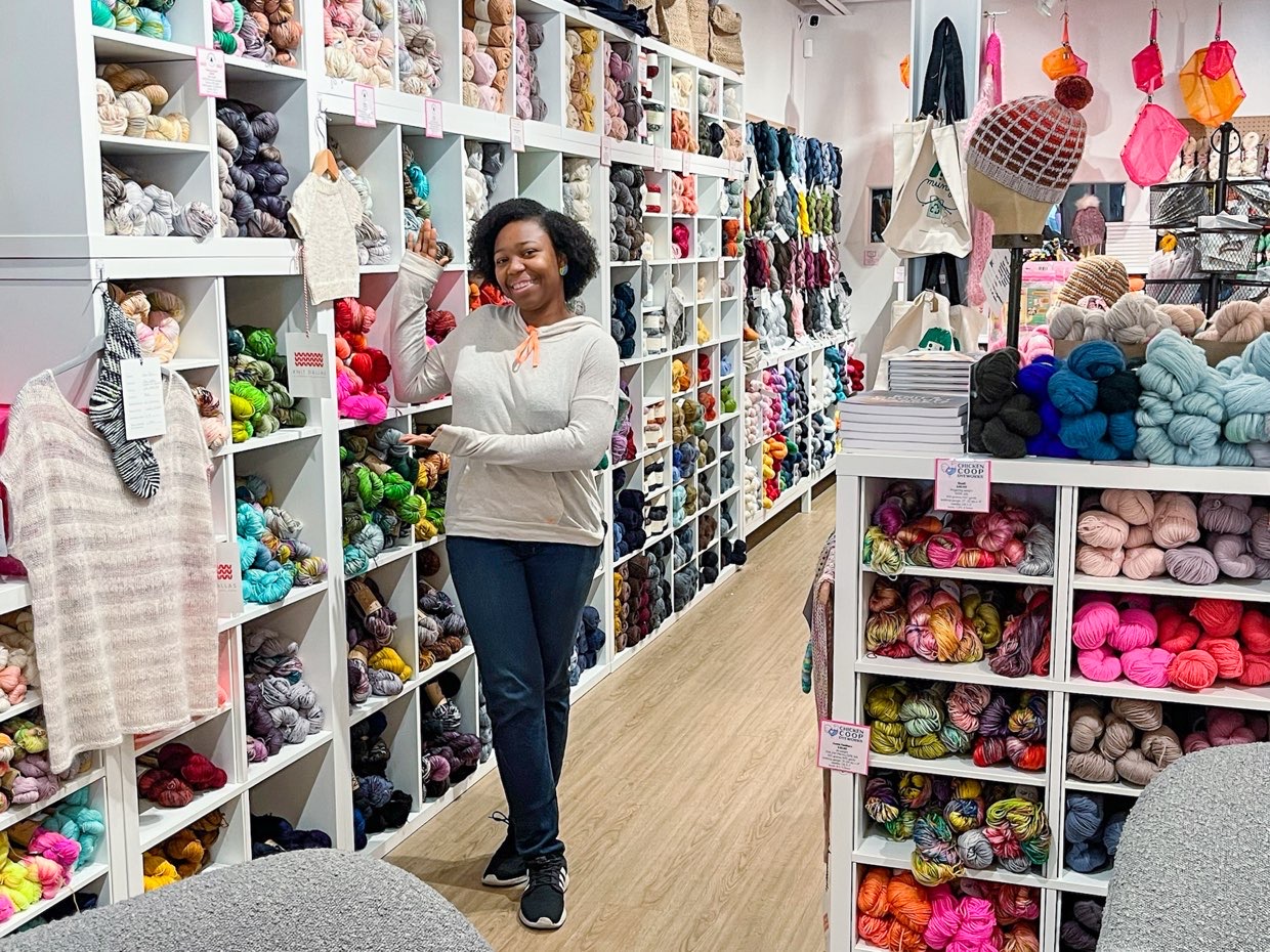young lady pointing at beautiful cabinet of yarns at dfw yarn crawl