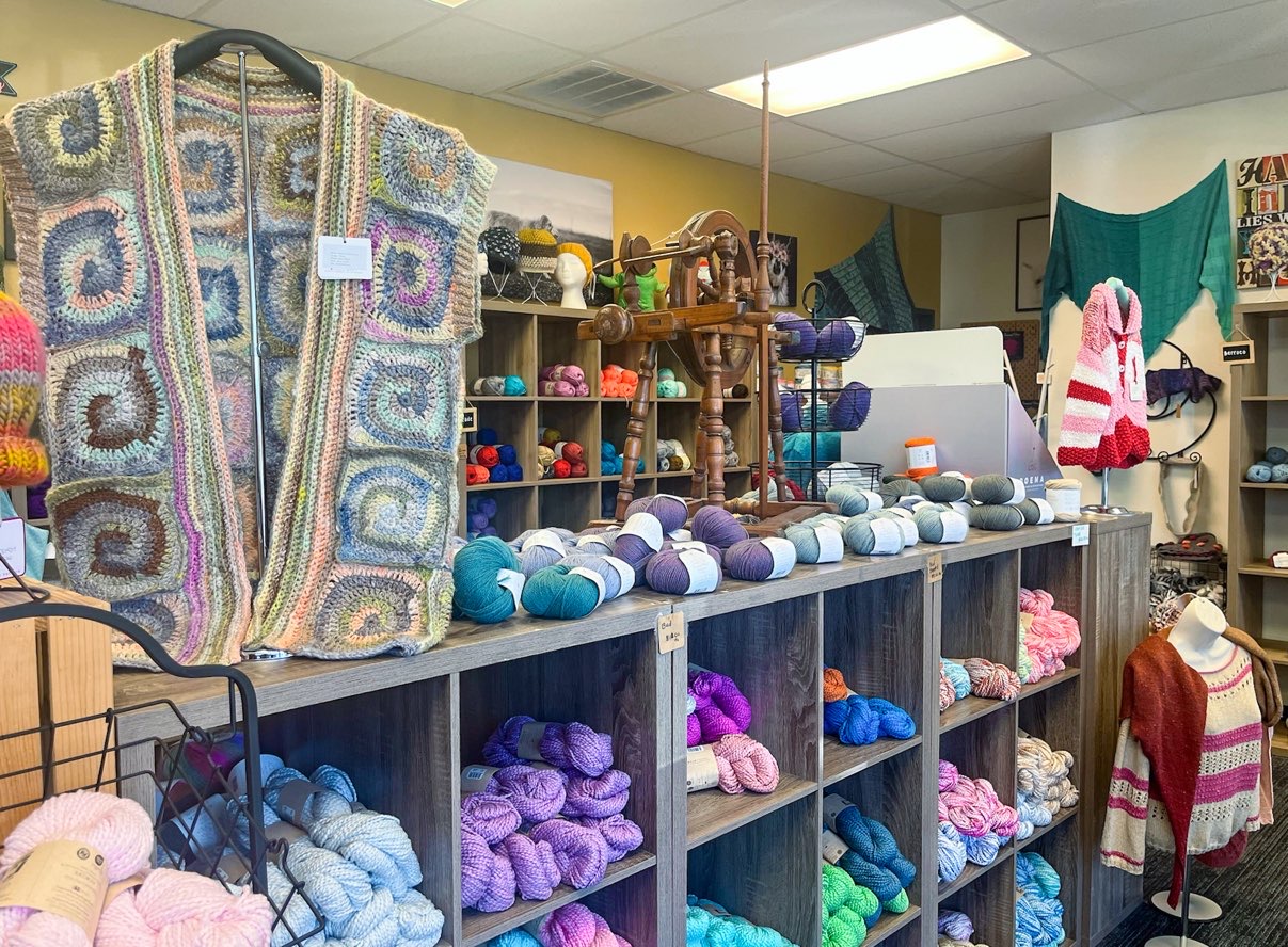 Cubbies full of beautifully colored skeins of yarn with hanging crocheted blanket at On The Lamb yarn shoppe