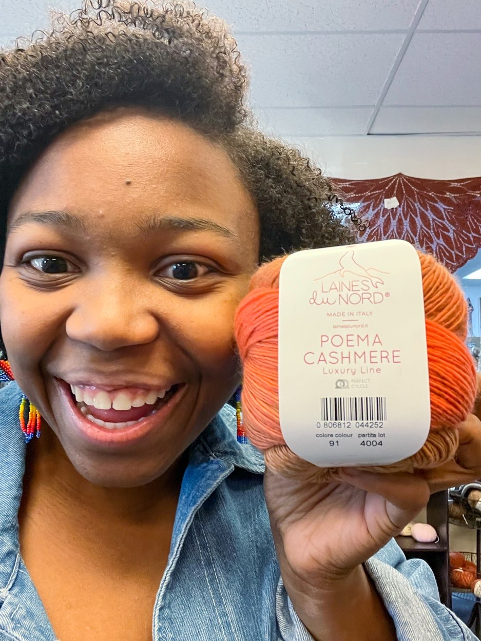 Smiling young lady holding up skein of rust colored yarn at North Texas Yarn Crawl