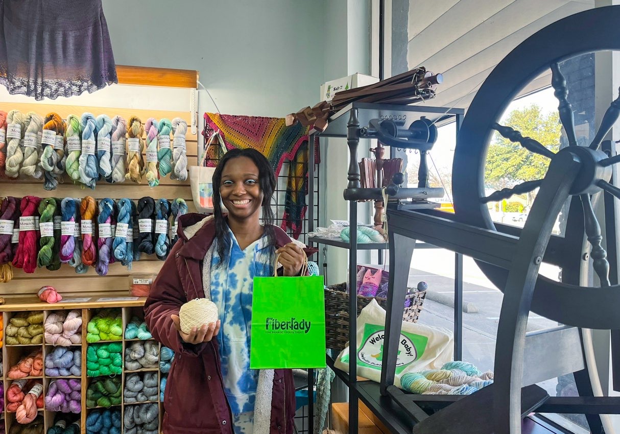 Young lady smiling cheerfully while holding off white ball of yarn;