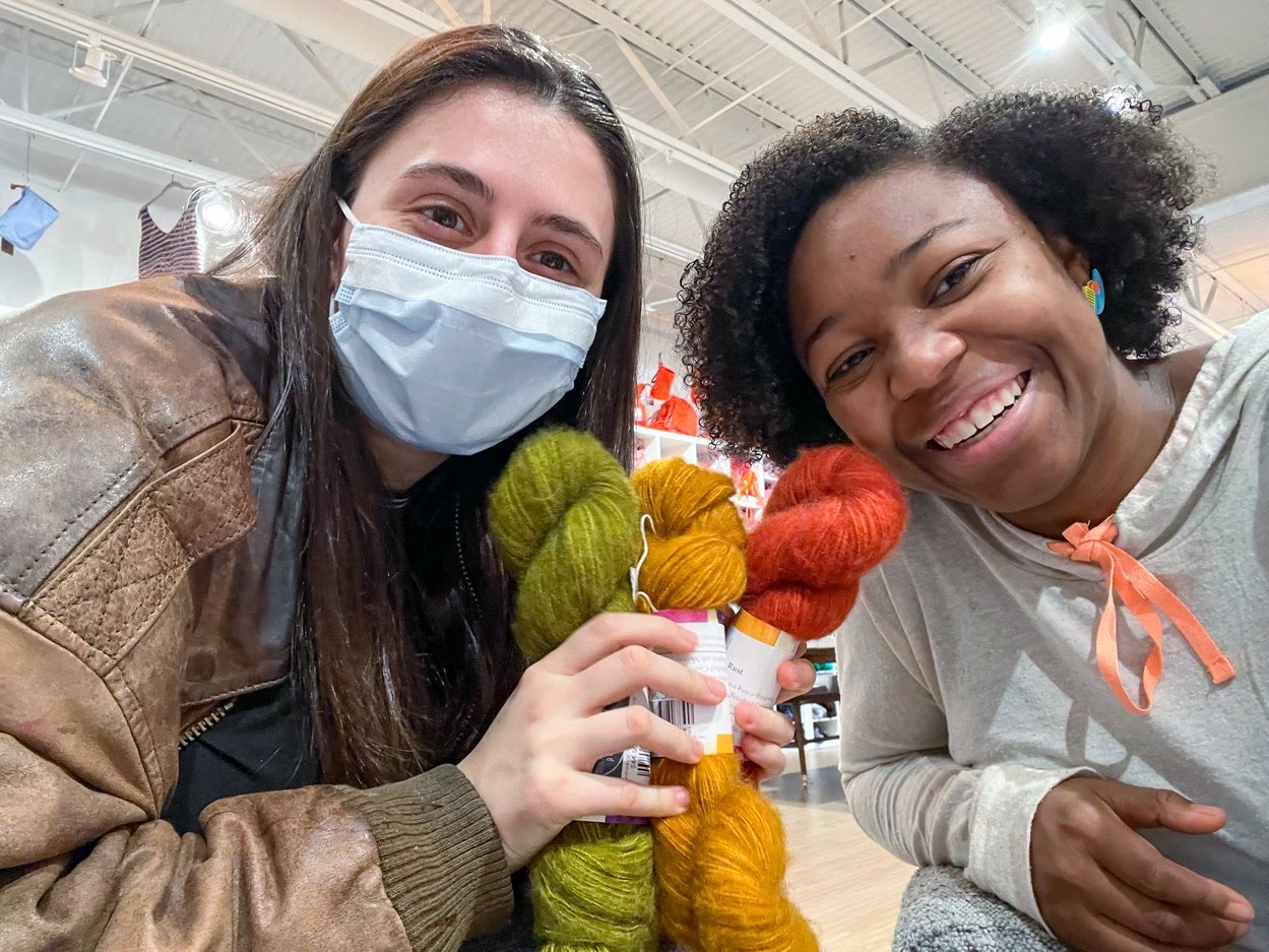 two young ladies holding green, gold, and rust, yarns at dfw fiber festival