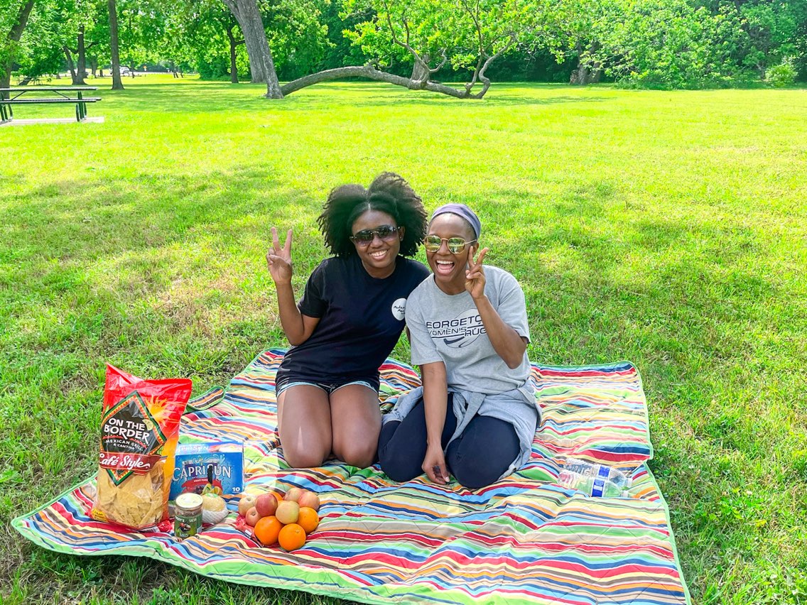 two young ladies sitting on picnicking at White rock lake park. is dallas texas worth visiting? Yes