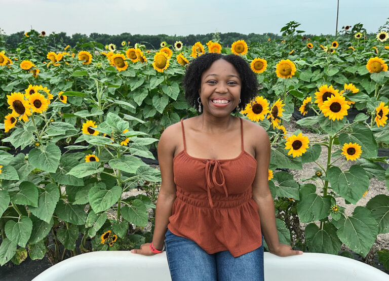 A woman smiling while posing in front of blooming sunflowers at a sunflower field near Dallas.