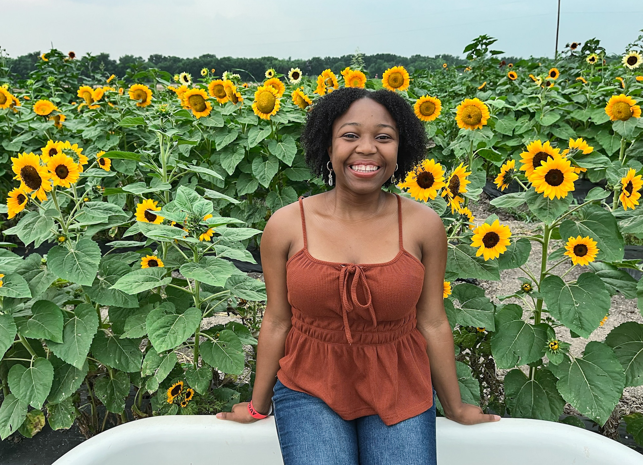 A woman smiling while posing in front of blooming sunflowers at a sunflower field near Dallas.