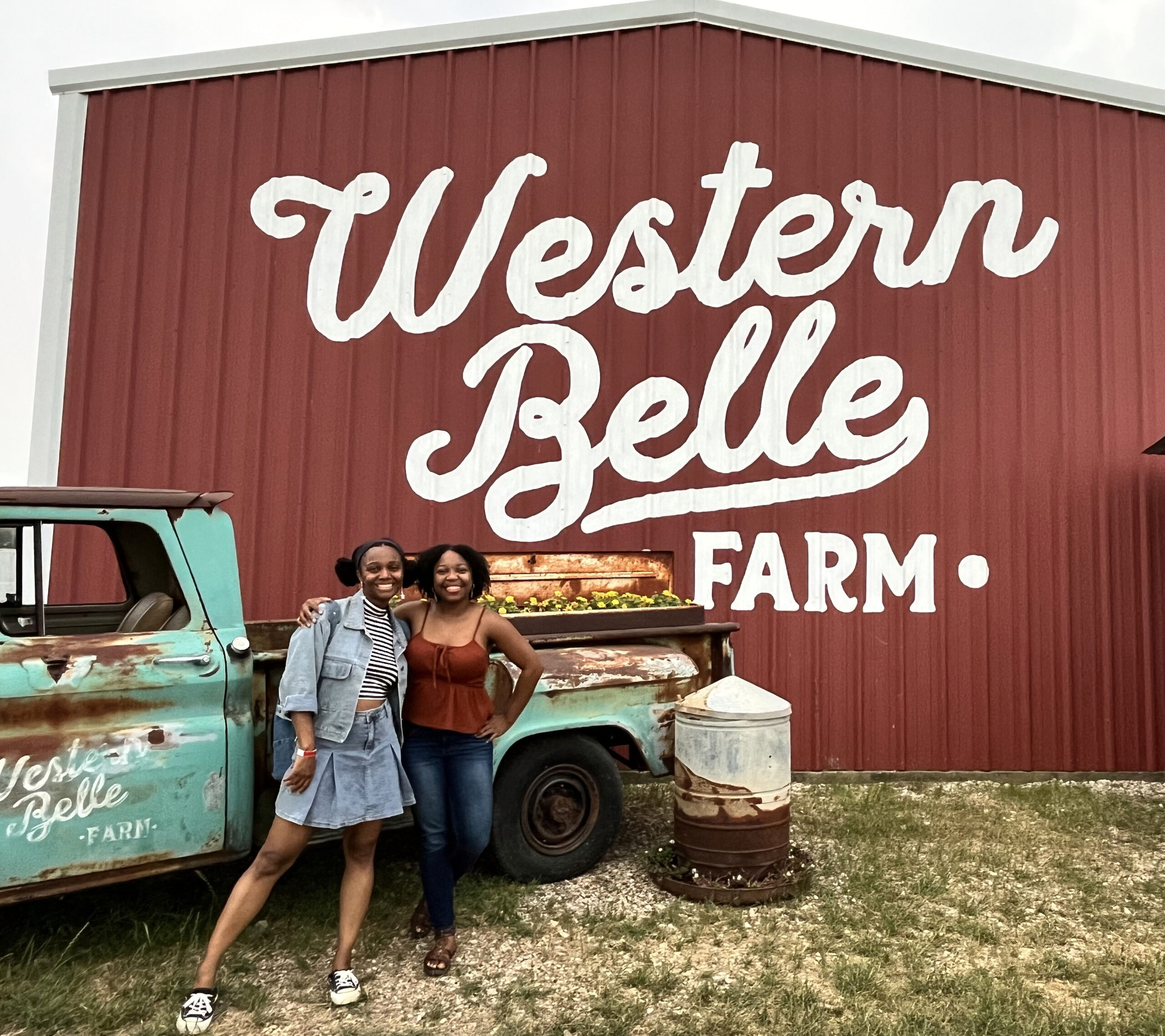 Two women standing in front of an old work truck and barn at a sunflower farm near Dallas.