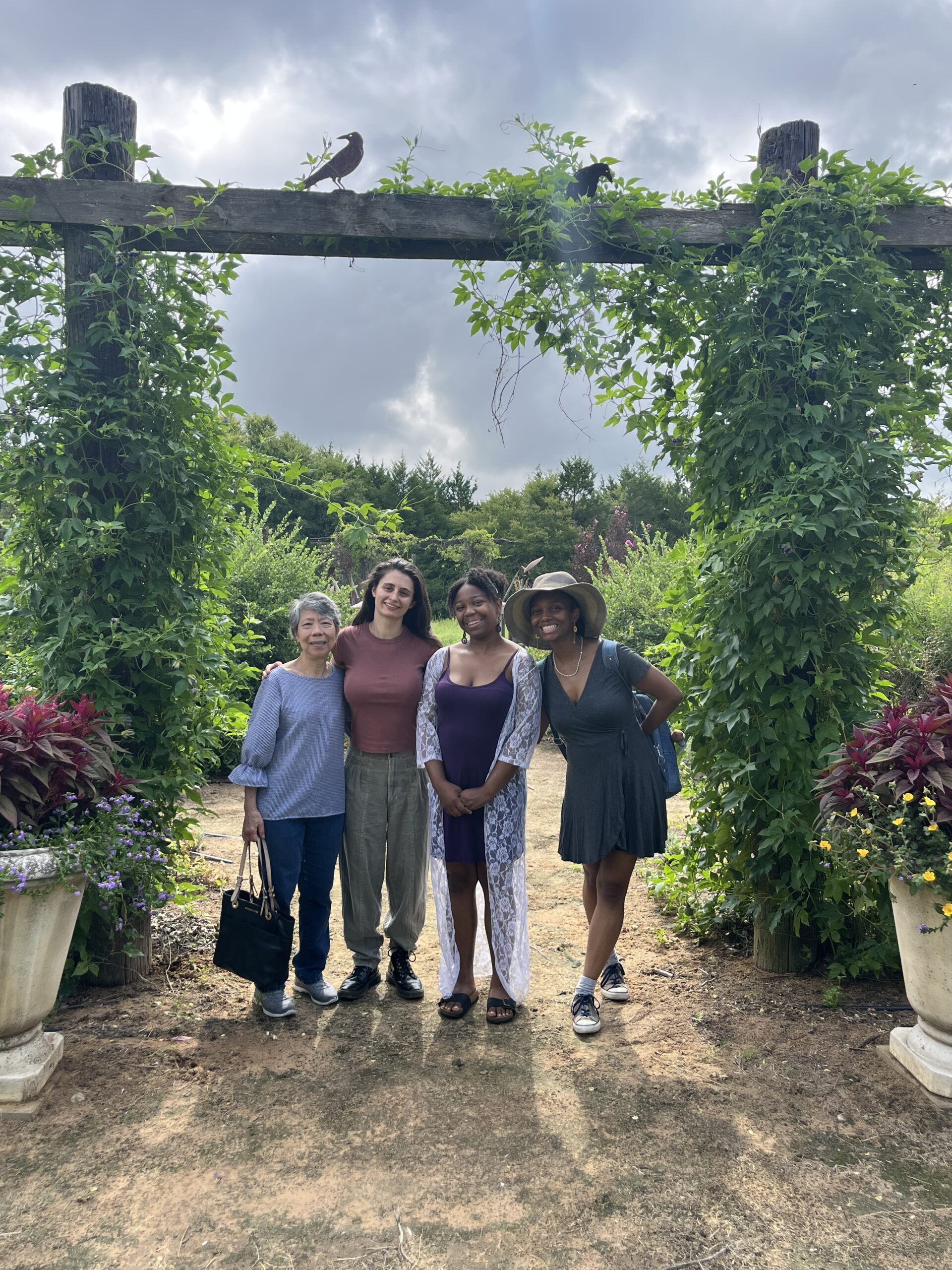 A group of women standing under a square arch of green vines with birds perched on top at Lavender Ridge Farms in Texas.