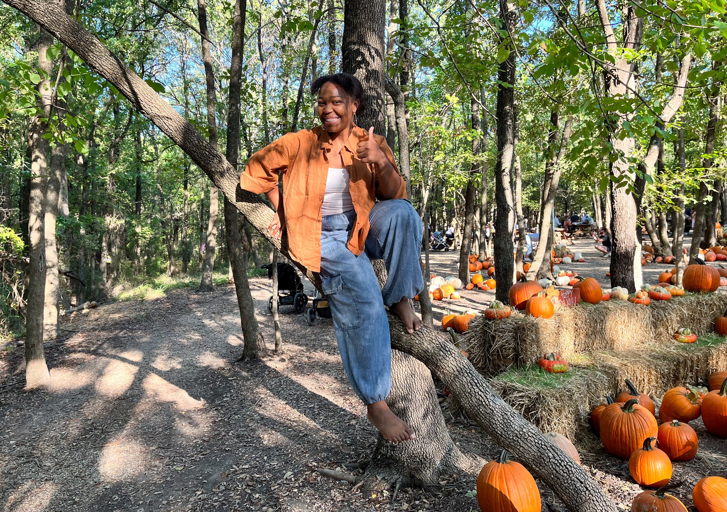 Young woman smiling while sitting barefoot in a tree at one of the many Dallas Farms near Dallas, Texas.