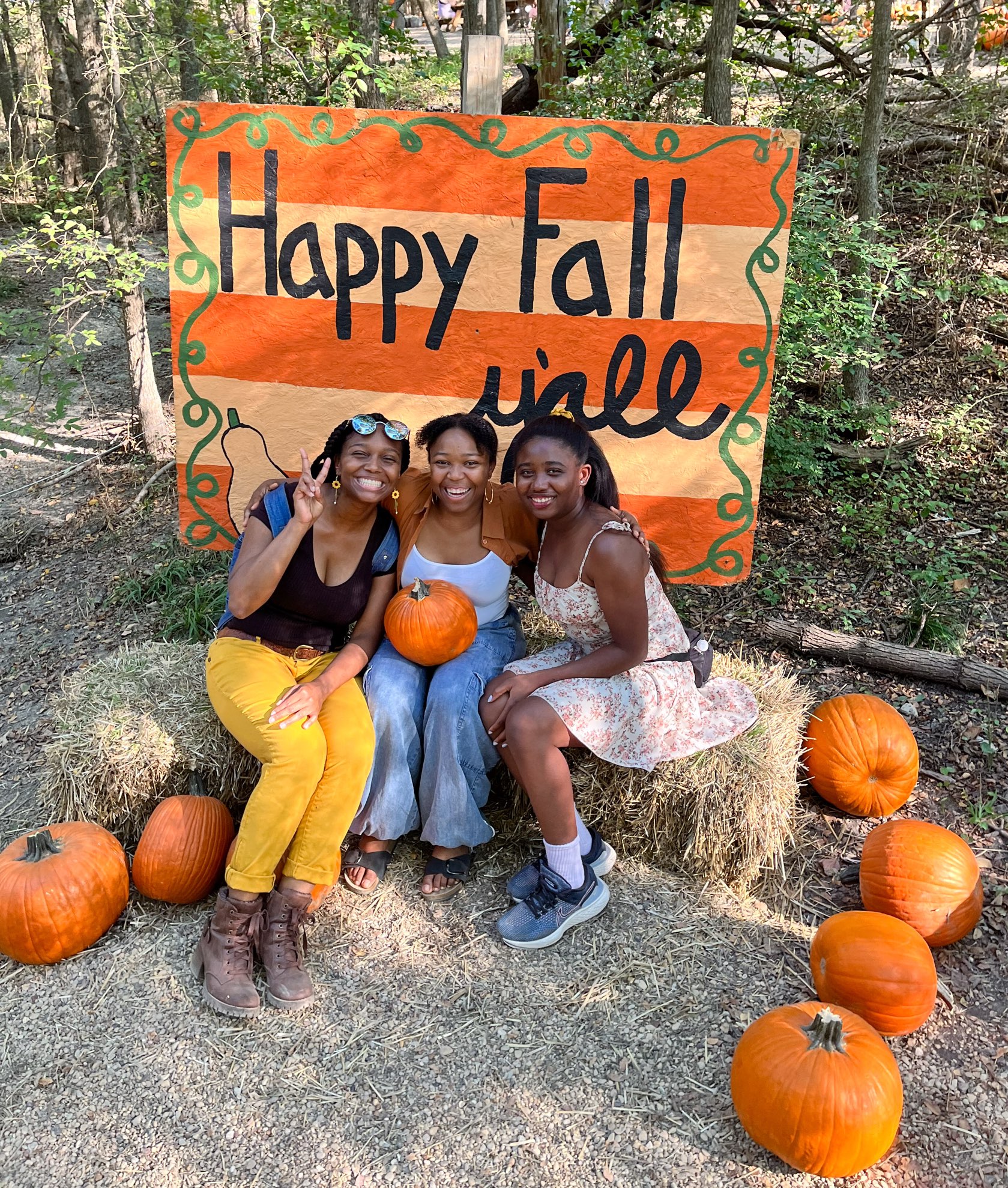 Three young ladies pose with pumpkins in front of a ‘Happy Fall Y’all’ sign at Blase Family Farm, one of the many Dallas Farms near Dallas, Texas.