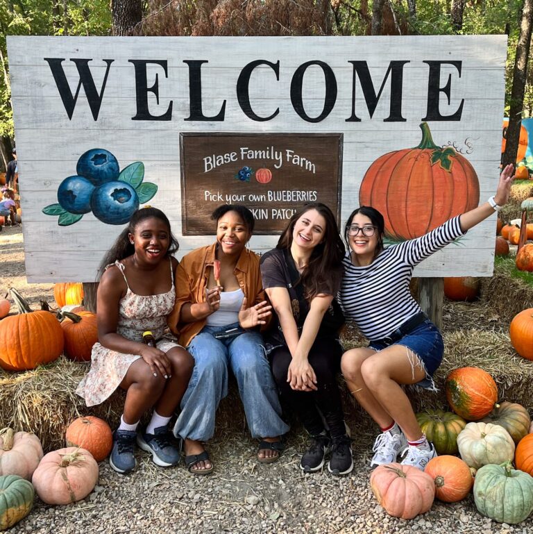Young ladies enjoying the pumpkin patch at Blase Family Farm, posing in front of the welcome sign