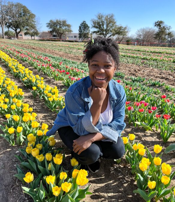 Young woman squatting among rows of yellow tulips in a Texas tulip field.