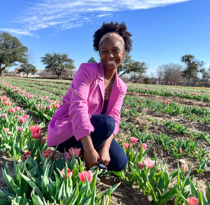 Young lady crouches in a Texas tulip field surrounded by pink tulips.