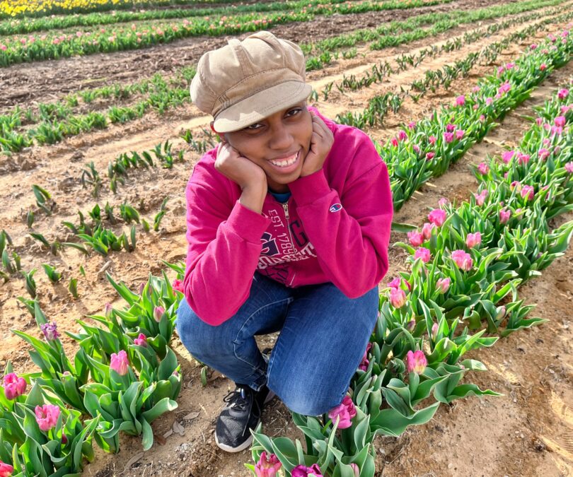 Young lady squats in a Texas tulip field among rows of pink tulips.