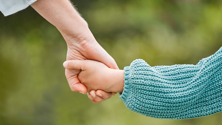 Parent holding the hand of a child while walking outdoors, one of the free things to do in Dallas with kids.