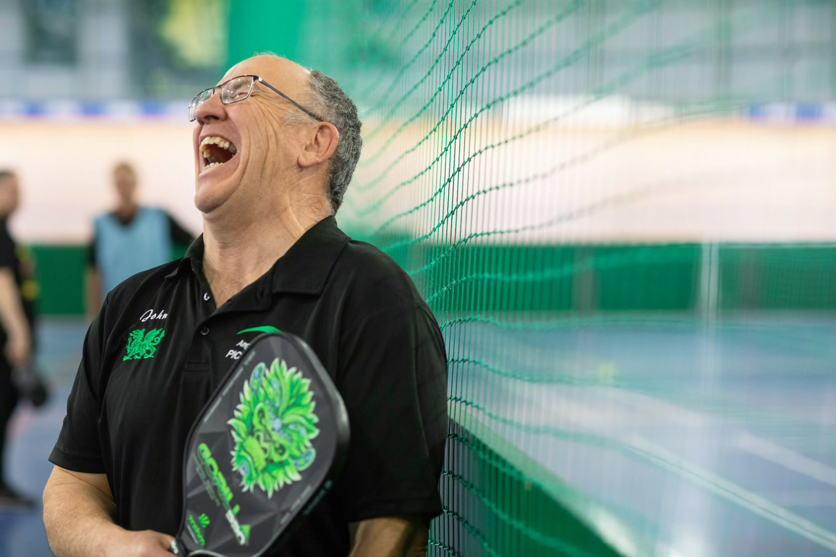 Middle-aged man laughing while holding a pickleball paddle, representing beginner-friendly Dallas sports leagues