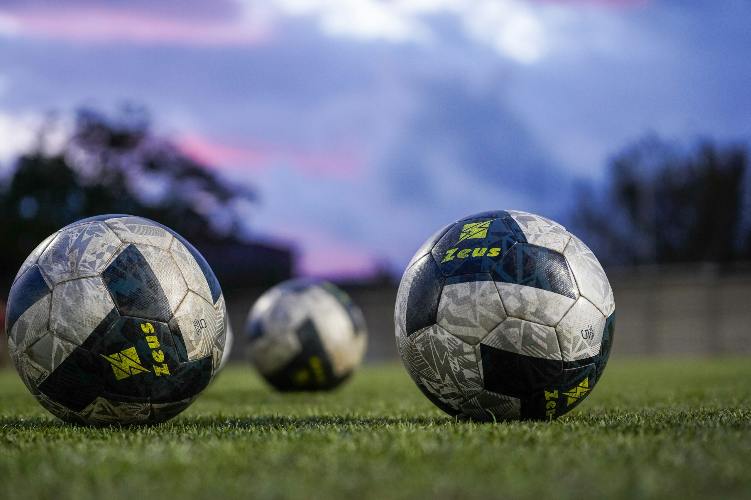 Three soccer balls on astroturf field, highlighting adult soccer leagues in Dallas sports leagues
