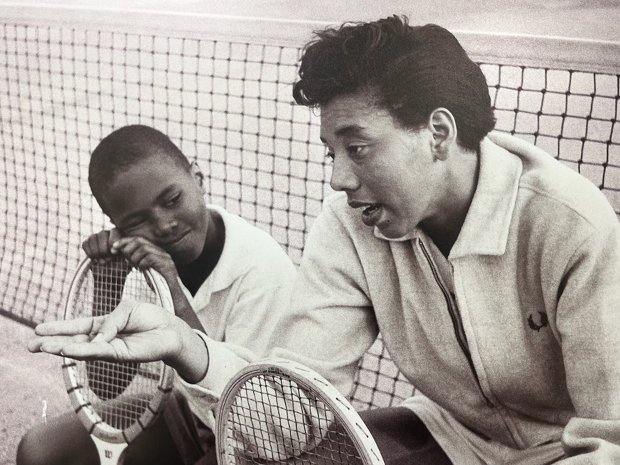 Tennis player speaks to young boy at a tennis court setting, featured in African American Museum of Dallas reviews.