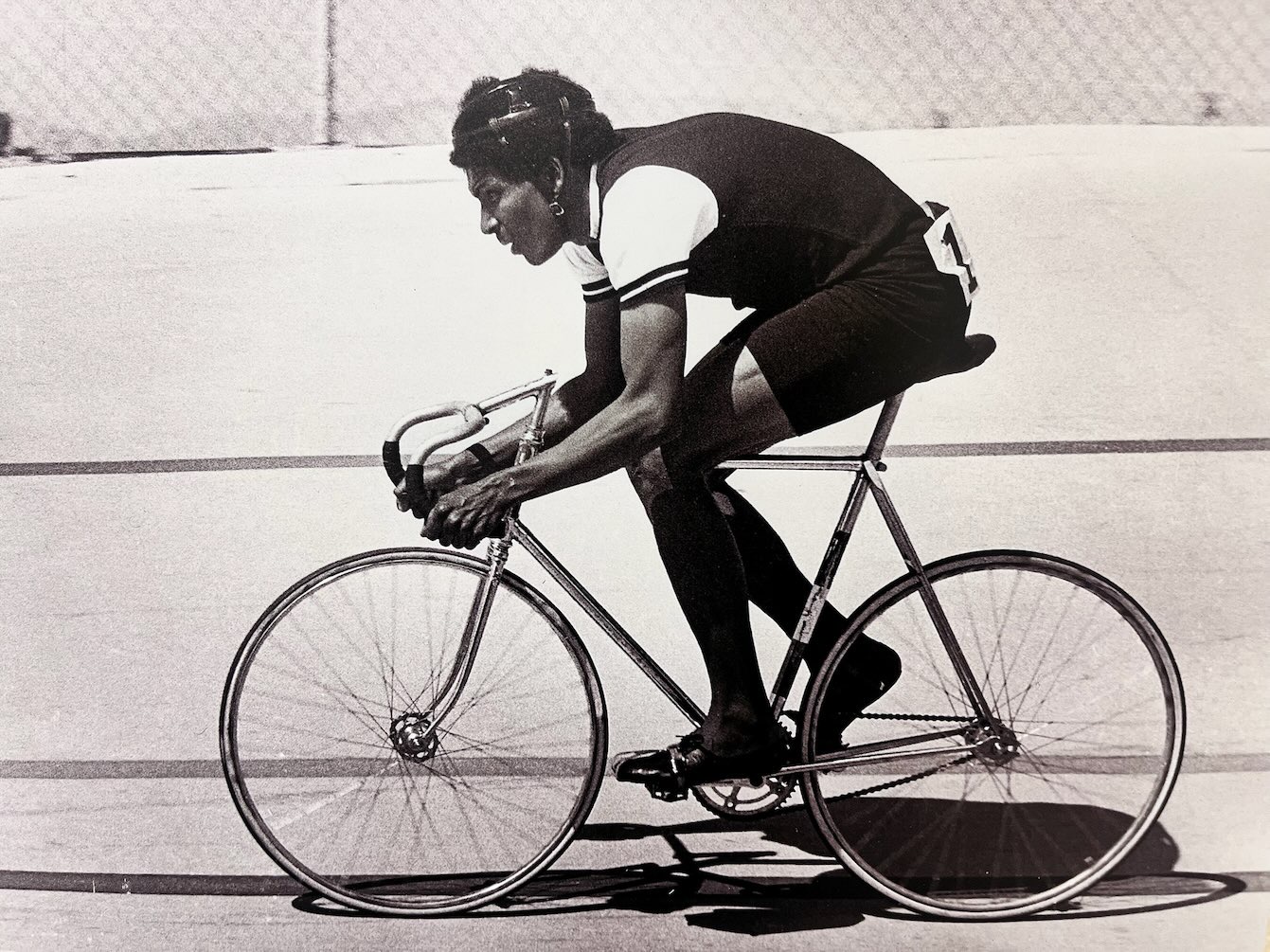 Man in cycling racing attire rides a bicycle in a forward racing position with hands firmly on the handlebars and legs in motion, featured in African American Museum of Dallas reviews.