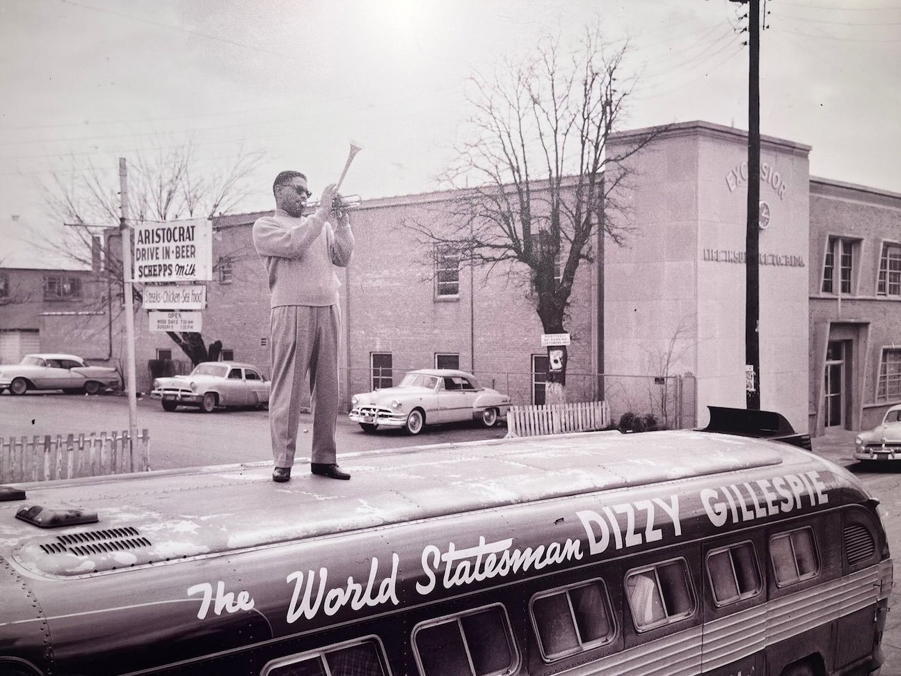 Dizzy Gillespie stands on top of a bus playing trumpet in a lively performance scene, featured in African American Museum of Dallas reviews.