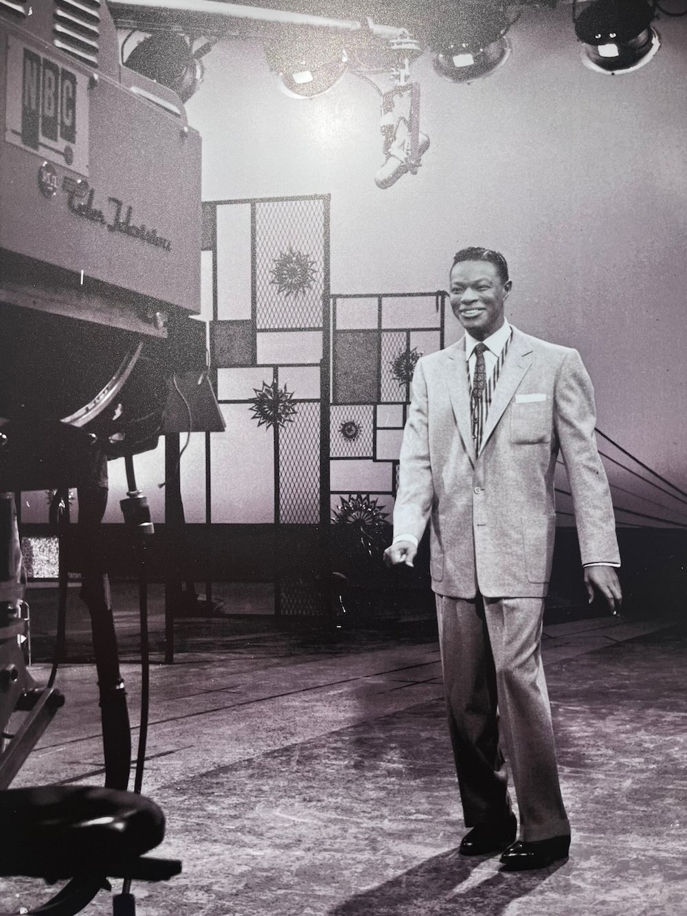 Nat King Cole performs while smiling and looking forward toward the camera, featured in African American Museum of Dallas reviews.
