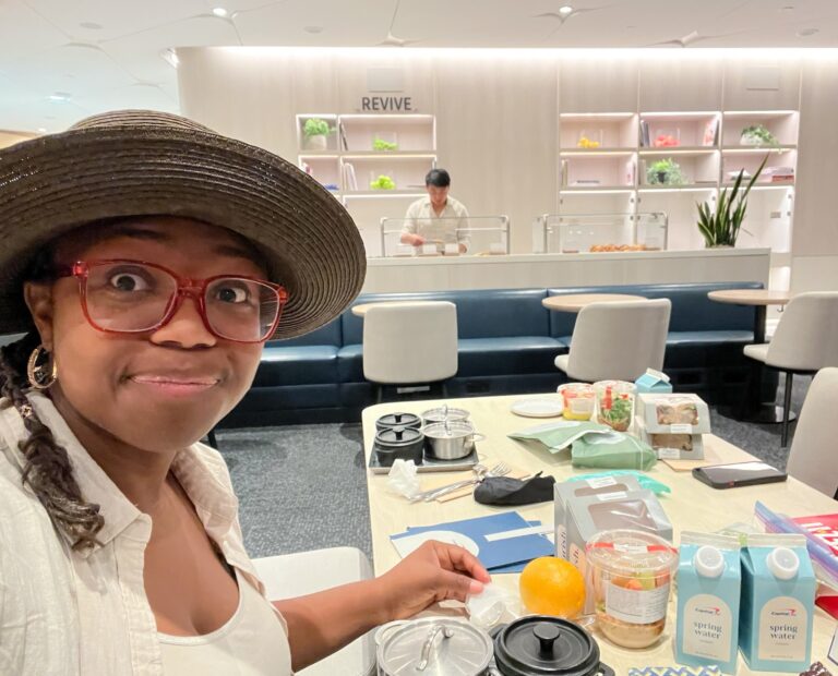 Young woman dining inside the Capital One Lounge at DFW Airport with bowls of fresh food, snacks, and to-go goodies at her table in one of the best Dallas airport lounges.