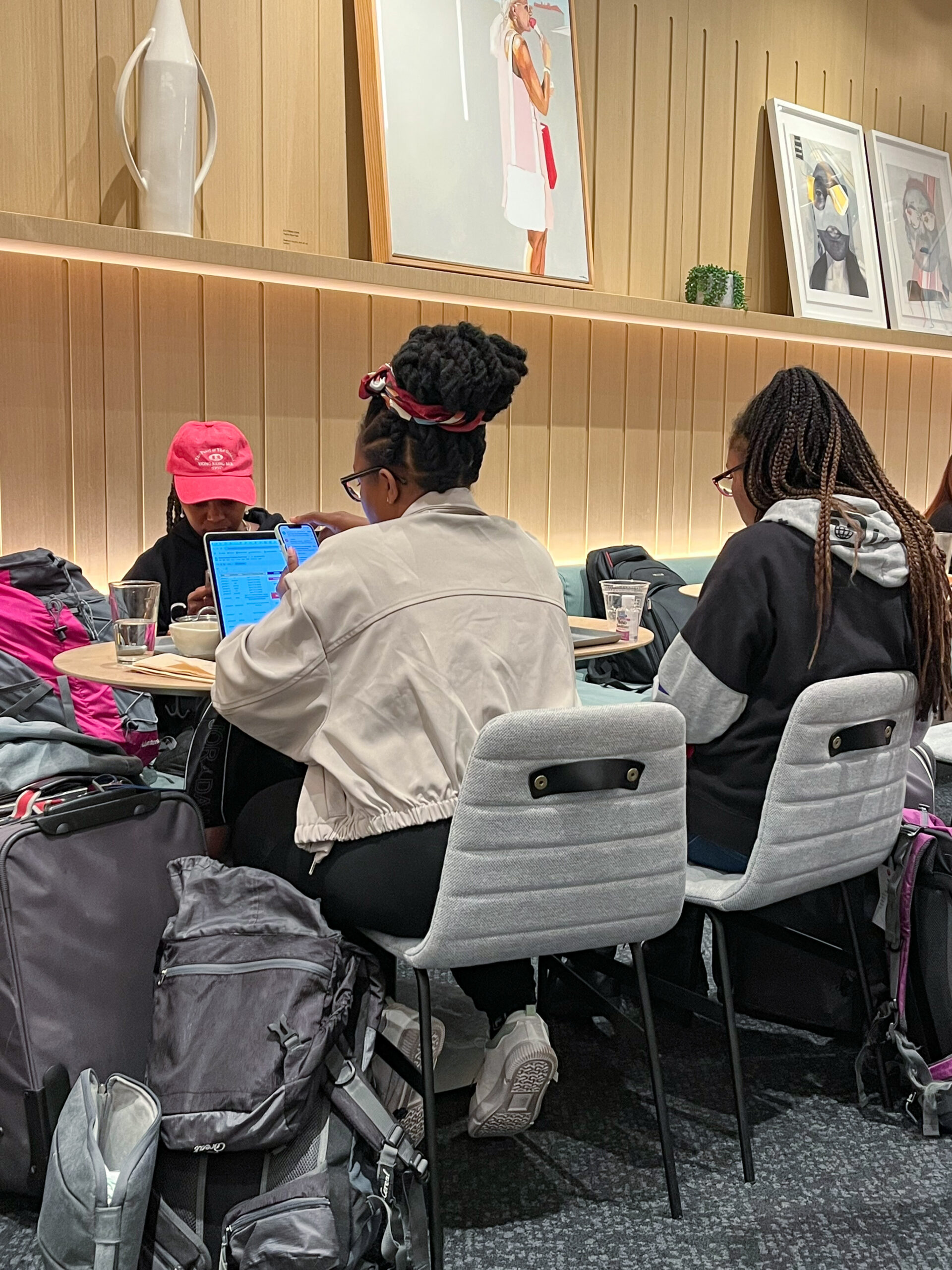 Three young women relaxing at a table inside the Capital One Lounge at DFW Airport while waiting for their flights at one of the most popular Dallas airport lounges.