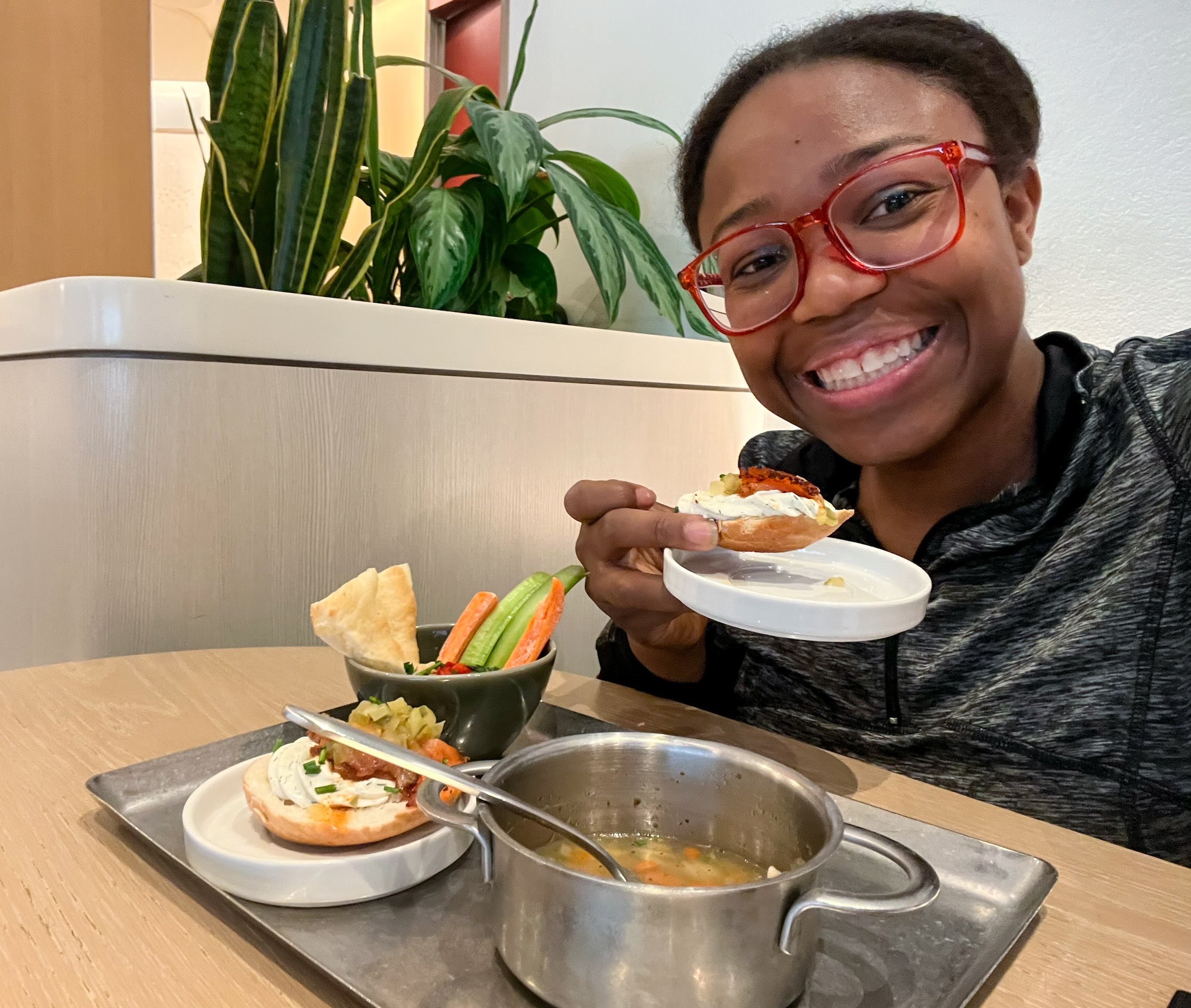 Young woman smiling at the camera while enjoying food inside the Capital One Lounge at DFW Airport, one of the Dallas airport lounges.