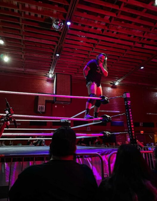 DFW wrestling performer standing on the corner ropes at Smash Mouth Wrestling in Haltom City looking out at the crowd