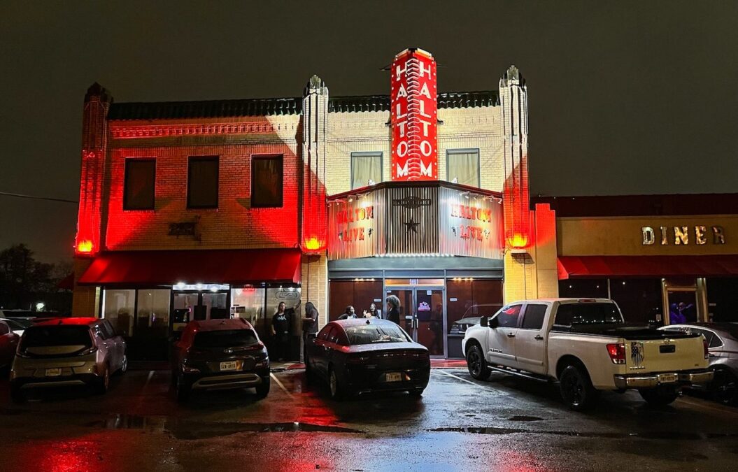 Haltom City Theatre exterior at evening during a DFW wrestling event with cars parked outside and lights illuminating the building