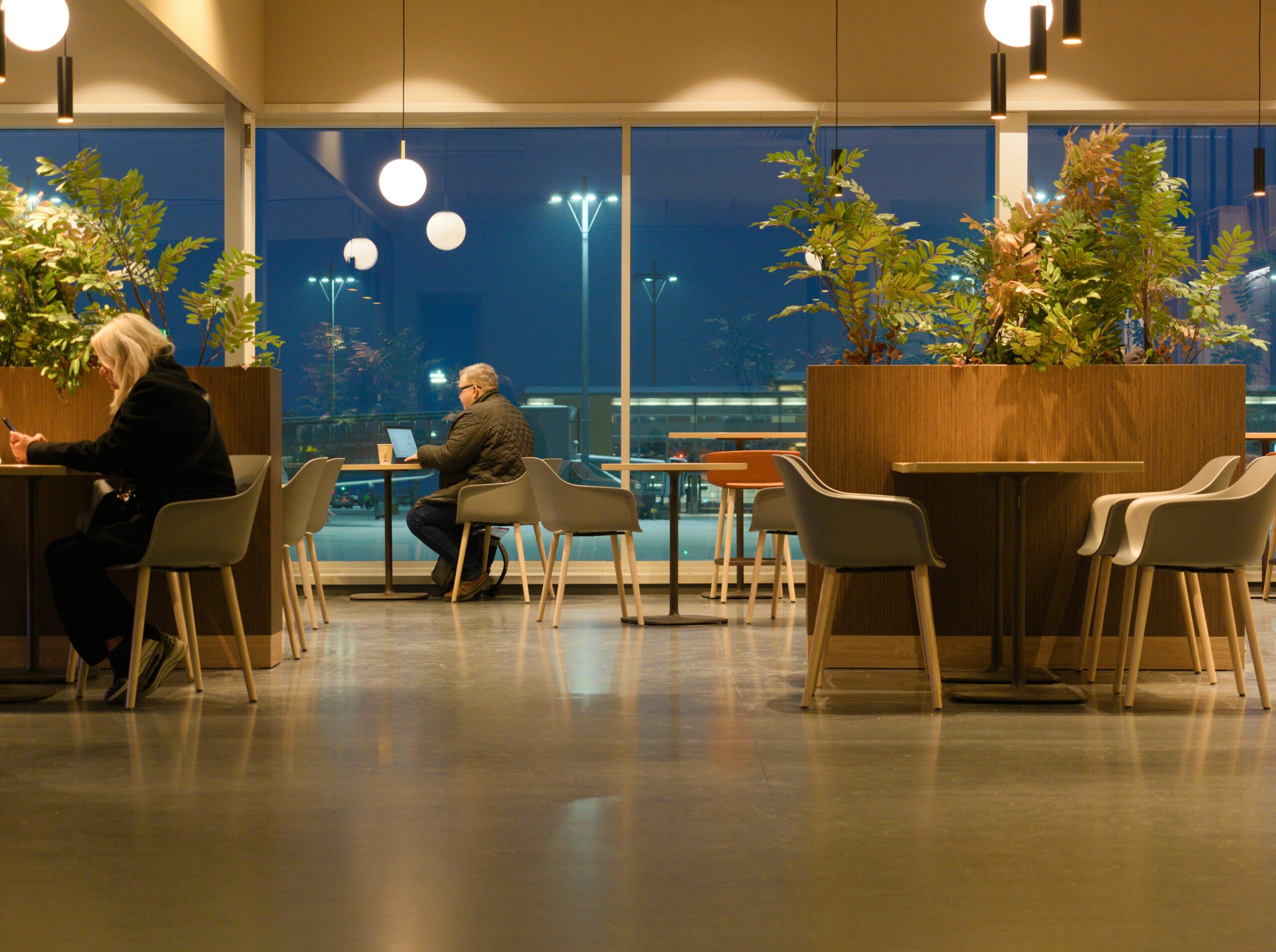 Man working on a laptop while a woman checks her phone inside one of the Dallas airport lounges at DFW Airport.