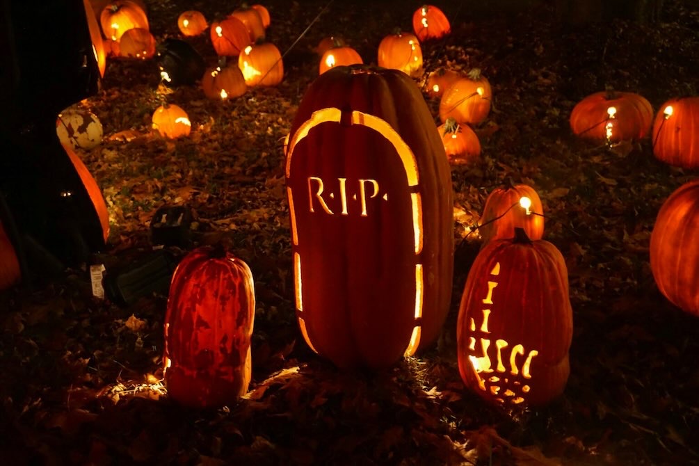 Carved pumpkins arranged in a graveyard scene with a lit “R.I.P.” pumpkin at Pumpkin Nights.