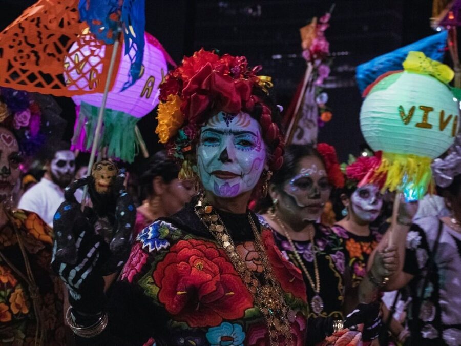 People in colorful costumes and skull face paint celebrating Día de los Muertos at a Dallas fall festival.