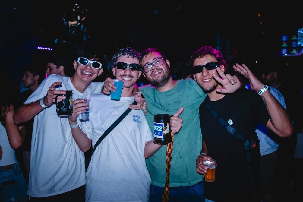 Four young men smiling, raising beer cups, and posing at a Dallas fall event in Deep Ellum.