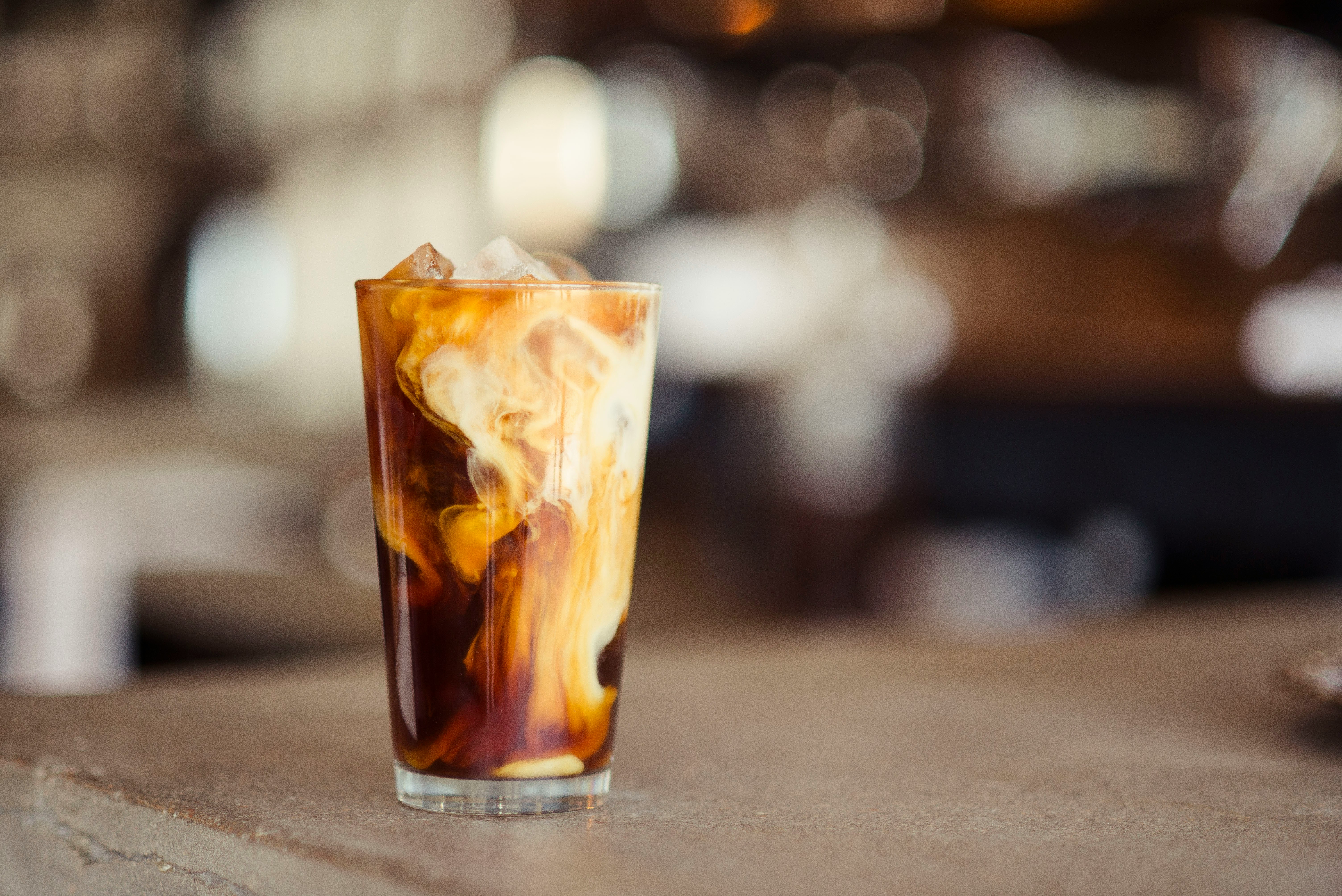 Tall glass of iced coffee with milk swirling through the coffee and ice cubes rising above the rim.