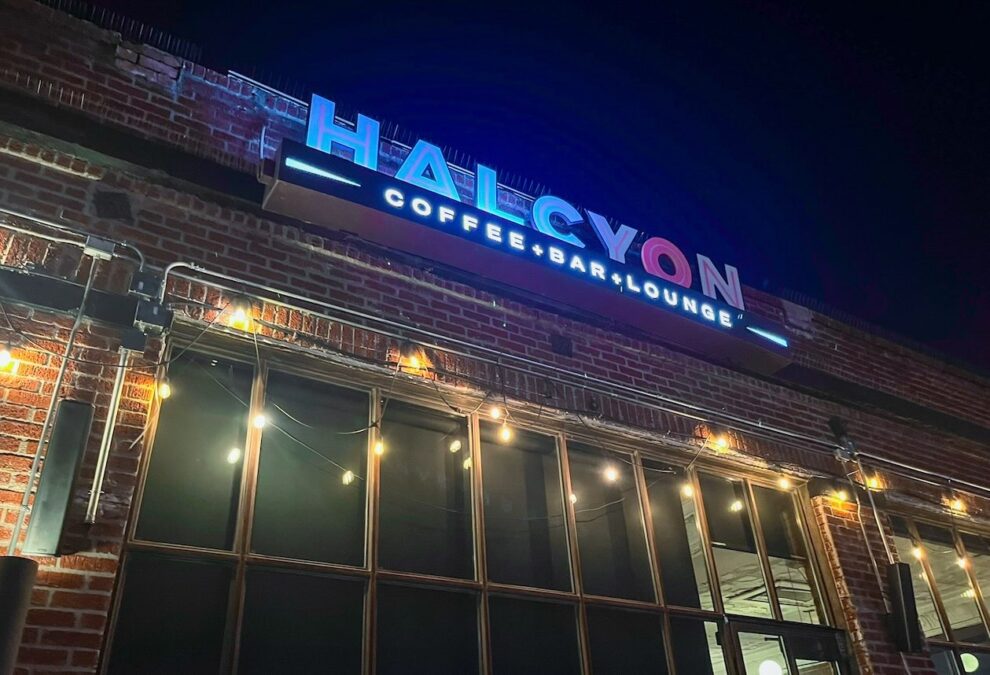 Illuminated Halcyon Coffee Bar & Lounge sign on a brick building with multi-paned front windows at one of the late-night coffee shops in Dallas.