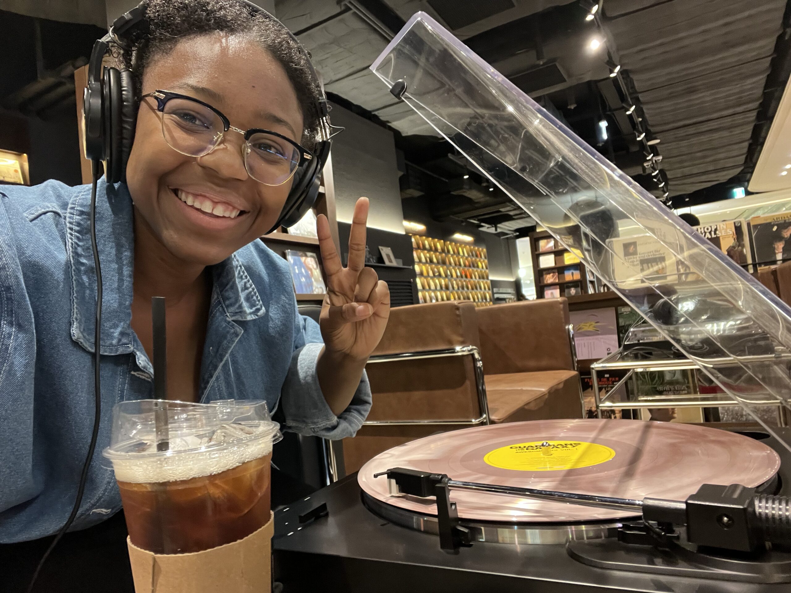 The writer of this late-night coffee shops in Dallas guide smiles and flashes a peace sign beside a vinyl record player at a Dallas coffee shop.