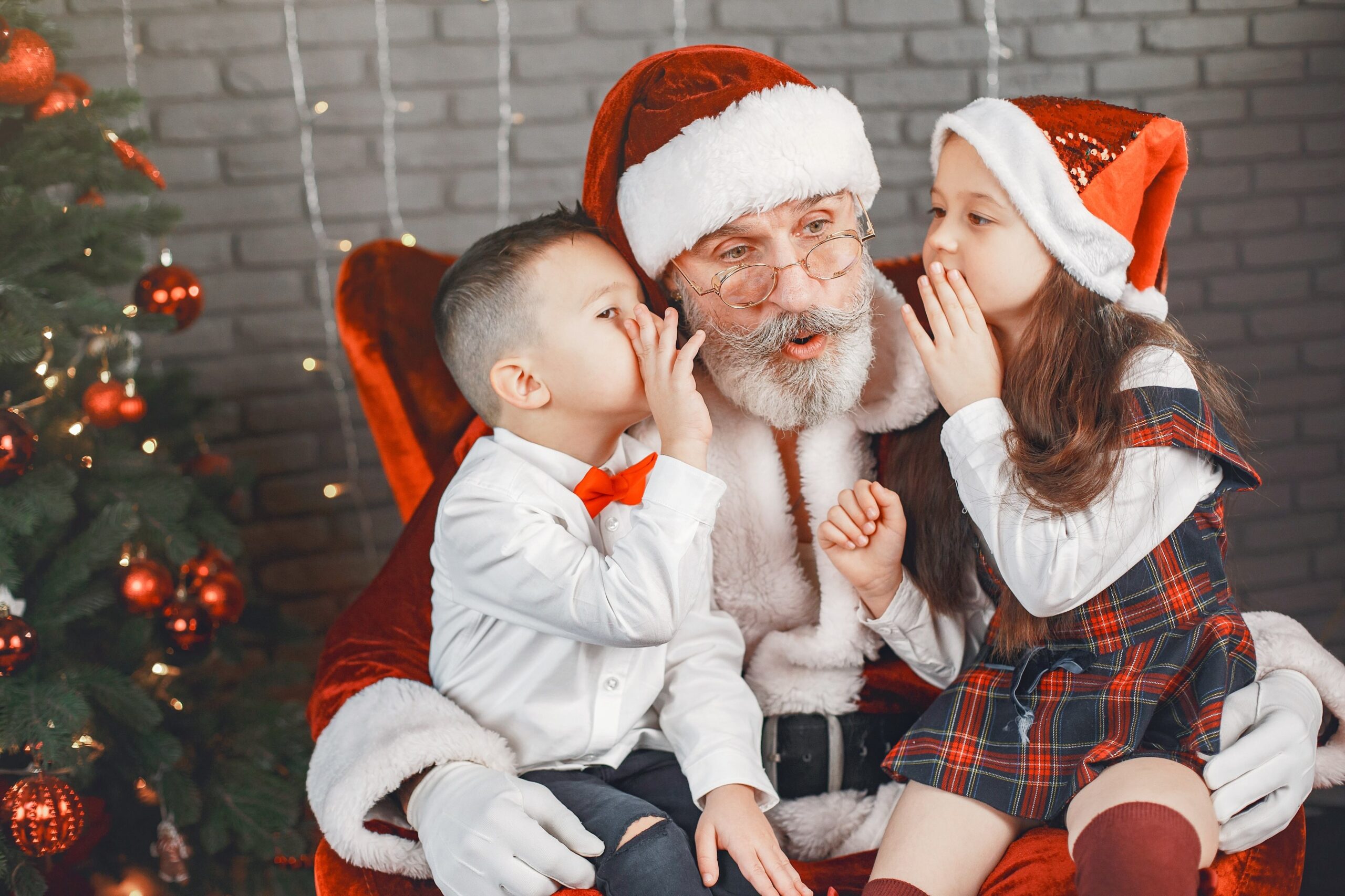 Santa listens as a young brother and sister sit on his lap, one on each leg, whispering in his ears during Christmas in Grapevine.