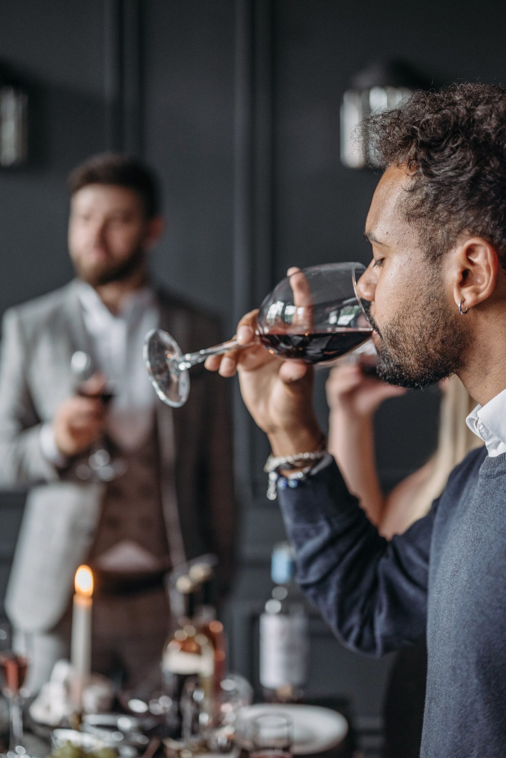 Man enjoys a glass of red wine at a Grapevine wine venue during Christmas in Grapevine, with other guests and wine glasses softly blurred in the background.