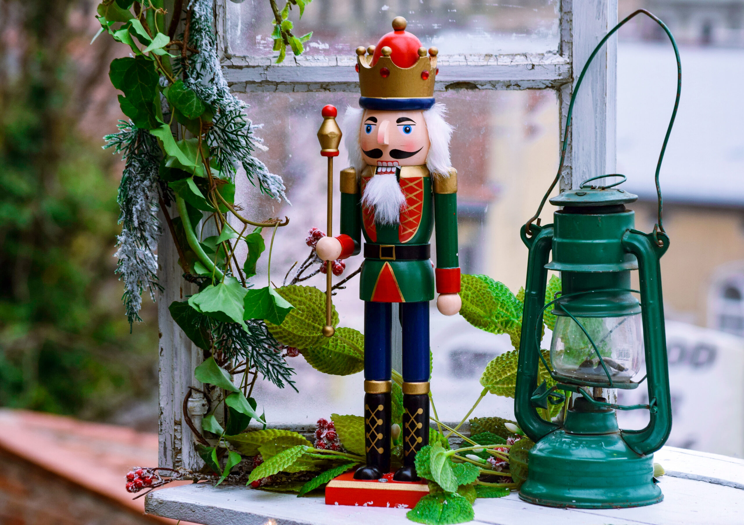 Christmas in Grapevine toy soldier in green and red uniform stands beside a festive lantern decorated with frosted greenery.