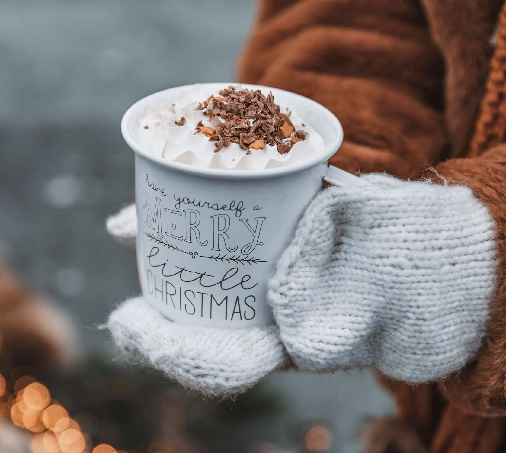 Mitten hands hold a cup of hot cocoa topped with whipped cream and chocolate shavings during Christmas in Grapevine.