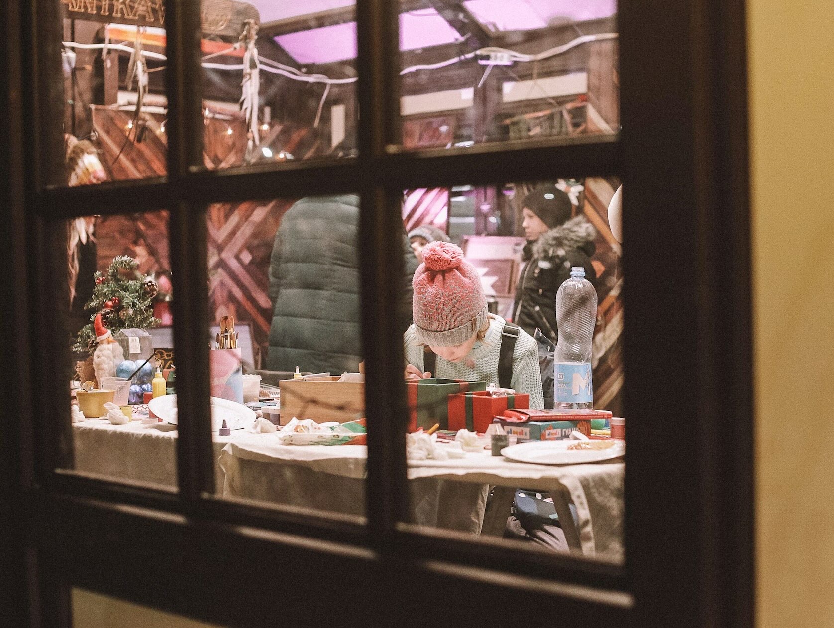 A young girl looks into a gift box while holiday shopping, viewed through the paned windows of a store during Christmas in Grapevine.