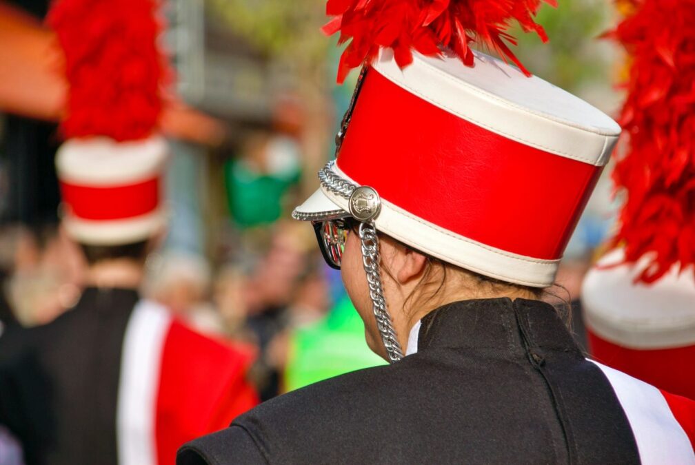 Winter in Dallas Christmas parade performer in a red and white band hat with a feather plume, standing in formation with her marching band.